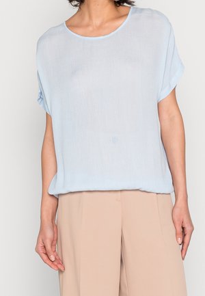 Lyseblå kortærmet bluse lavet af et let materiale, med rund halsudskæring og oprullede ærmer, parret med beige bukser.