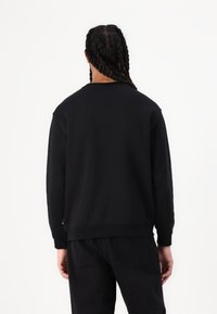 Schwarzes Sweatshirt mit Rundhalsausschnitt, langen Ärmeln und gerippten Bündchen. Die Rückseite ist schlicht ohne sichtbare Logos oder Muster.
