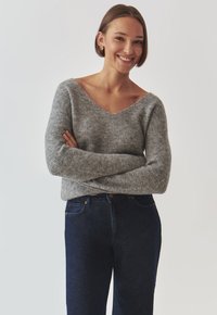 Grå striktrøje med V-udskæring, ribbet tekstur og lange ærmer, parret med mørkeblå denimjeans. Simpelt design, ingen mønstre eller accenter.