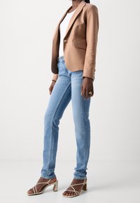 Beige skräddarsydd kavaj med guldknappar, vit topp, ljusblå jeans och beige sandaler med klack. Slät tyg och avslappnad passform.