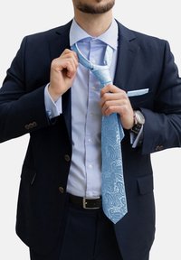 Šviesiai mėlynas paisley tipo kaklaraištis, pagamintas iš šilko, derinamas su tamsiai mėlynu kostiumu ir šviesiai mėlyna marškiniu. Yra subtilių raštų ir derančio kišeninio squares.