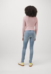 Suéter de punto rosa claro combinado con jeans ajustados azul claro y zapatillas blancas con acentos amarillos, visto desde atrás.