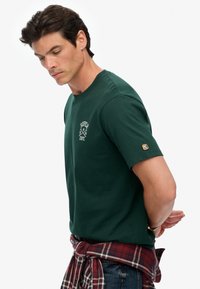 Groen katoenen t-shirt met een klassieke ronde hals. Heeft een witte bedrukte logo op de borst en een klein merkembleem op de mouw.