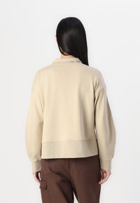Felpa beige con collo alto, polsini e orlo a costine. Texture liscia e vestibilità comoda, abbinata a pantaloni cargo marroni.