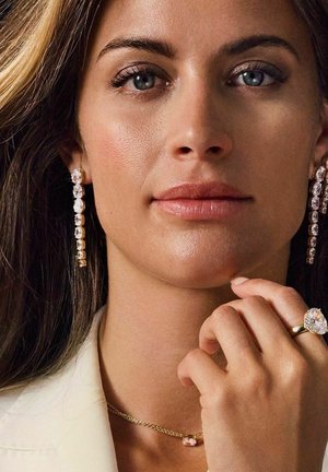 Guldøreringe med klare ædelsten, en delikat guld kædedyse med en pink ædelsten, og en stor ring med en oval klar sten.