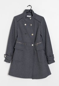 Grå uldfrakke med dobbeltradet design, sølvknapper, flade lommer og justerbare manchetter. Har en lynlåsdetaile ved taljen.