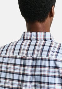 Plaid button-up shirt featuring blue, navy, and red colors. Soft fabric with a classic collar and back yoke detailing.