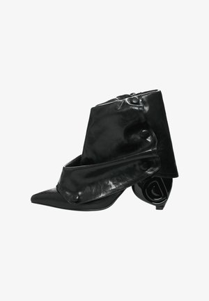 Bottine en cuir noir à bout pointu, avec un design replié et des accents de boutons. Talon courbé et brillant avec une forme unique.