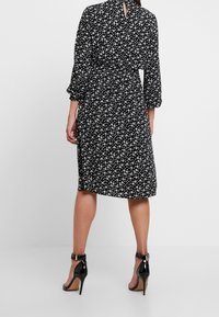 Svart klänning med vitt blommönster, trekvartsärmar, cinchad midja och detalj med nyckelhål i ryggen. Kombinerad med svarta högklackade sandaler.