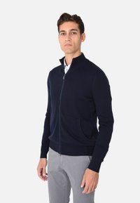 Maglione zip-up blu navy con colletto alto, polsini e orlo a coste, con tasca frontale, realizzato in materiale a maglia testurizzato.