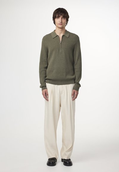 Gebreide olijfgroene pullover met een kraag en ritssluiting, gecombineerd met crèmekleurige wijde broek en zwarte leren schoenen.