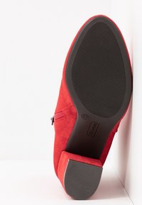 Bottine en daim rouge avec un talon plat, semelle en caoutchouc avec rainures texturées, et une fermeture éclair latérale pour un port facile. Étiquette taille 37 visible.