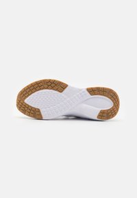 Witte sportbalschoen met een patroon in de rubberen zool; beschikt over een textuur voor grip en een contrasterende bruine buitenzool voor tractie.
