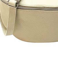 Ronde beige leren tas met een gestructureerd oppervlak, rits bovenkant en een enkele verstelbare schouderriem. Het ontwerp is compact en strak.