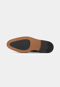 Suela de zapato de cuero negro con un inserto de goma marrón. Presenta una forma redondeada y un fondo texturizado para el agarre. Logo del fabricante grabado.