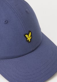 Casquette bleu marine en tissu ribbé avec un logo d'aigle brodé jaune sur le devant. Design à six panneaux avec des accents cousus.