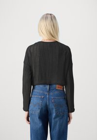 Zwarte cropped top met verticale ribbels, gecombineerd met high-waisted blauwe jeans met een leren merklabel en klassieke achterzakken.