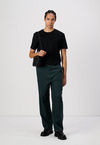 Sort bomulds T-shirt, grønne kordfløjl bukser, sorte støvler og en lille sort crossbody taske. Bukserne har lige ben og en struktureret overflade.