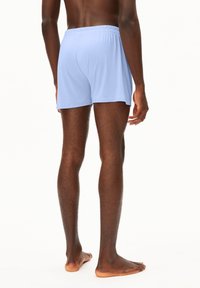 Helle blaue Baumwollshorts mit elastischem Bund, einfachem Design und lockerer Passform, von hinten gezeigt. Füße sind barfuß.