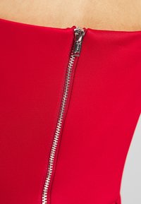 Red fitted garment featuring a zipper closure on the side, made of smooth fabric with a slight sheen. Zipper has metallic accents.
