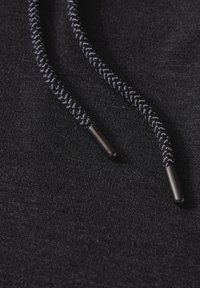 Gros plan sur un sweat à capuche noir avec un tissu texturé, des cordons tressés avec des accents gris clair et des embouts en métal noir.