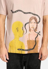 Light pink cotton t-shirt featuring a yellow figure and a woman with brown hair. Includes artistic text and a black abstract design element.