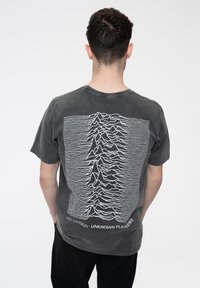 Dark grey cotton t-shirt featuring a white graphic design of waves and text "Joy Division • Unknown Pleasures" on the back. Round neckline.