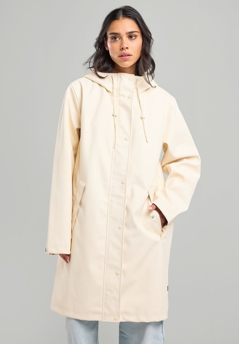 Cream waterproof jacket with a hood, snap buttons, drawstring, and side pockets; features a smooth texture and knee-length design.