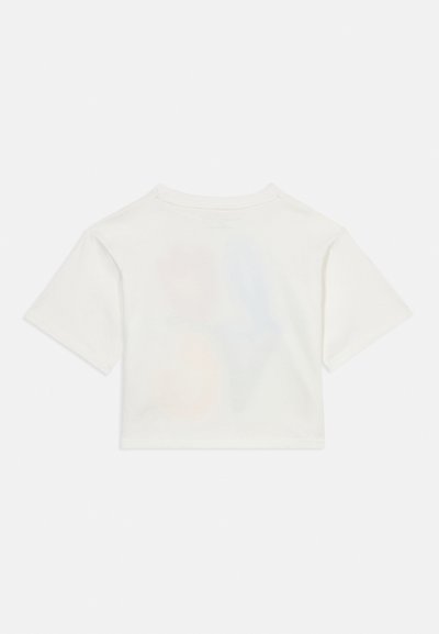 Vienkārša balta īsroku kropta T-krekls, novietots guļus, attēlots no aizmugures uz gaiša fona.