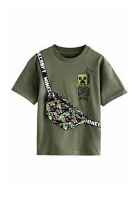 Olivegrünes Baumwoll-T-Shirt mit einem Minecraft Creeper- Grafik, kombiniert mit einer gemusterten schwarzen Gürteltasche, die verschiedene Spielcharaktere zeigt.