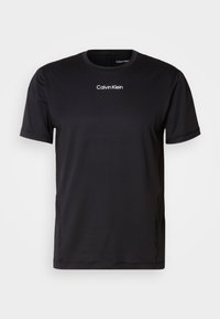 Czarna koszulka z krótkim rękawem wykonana z lekkiego materiału, z okrągłym dekoltem i białym logo "Calvin Klein" na piersi. Gładka tekstura.