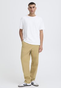 Maglietta bianca in cotone, vestibilità comoda, abbinata a pantaloni beige chiaro. Scarpe da ginnastica grigie e nere a righe completano l'outfit.