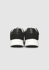 Scarpe da atletica nere con parte superiore in pelle liscia e camoscio, intersuola bianca e suola in gomma testurizzata, viste dal retro.