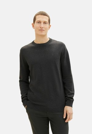 Suéter negro de tela suave, con cuello redondo y puños acanalados. Logo sutil en el pecho, combinado con pantalones oscuros.