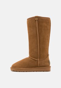 Botas de ante marrón hasta la rodilla con puntera redondeada y acabado texturizado. Presenta un botón decorativo en la parte superior y una suela de goma con tracción.