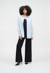 Ljusblå skjorta med knappar, svarta vida byxor och svarta klackskor. Skjortan är lös och byxorna har hög midja.