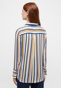 Striped long-sleeve shirt in blue, orange, yellow, and white. Features a collar and button cuffs, with a curved hem and smooth texture.