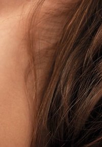 Welliges, strukturiertes braunes Haar, das an den Seiten kurz geschnitten ist, kombiniert mit einem glatten, hellen Hautton; die Highlights spiegeln eine subtile Tiefe und Glanz im Haar wider.