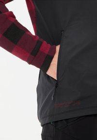 Fleece mouw in rood en zwart checkpatroon, zwarte body met een ritszak en lettering langs de zoom, gladde textuur, slim-fit ontwerp.