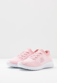 Světle růžové sportovní boty s texturovaným pleteným svrškem, bílou gumovou podrážkou a odpovídajícími tkaničkami. Na boku je logo a má pletený límec.