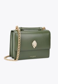Borsa a tracolla verde in pelle con una catena dorata, caratterizzata da una chiusura a conchiglia decorativa e dal nome del marchio in rilievo sul davanti.