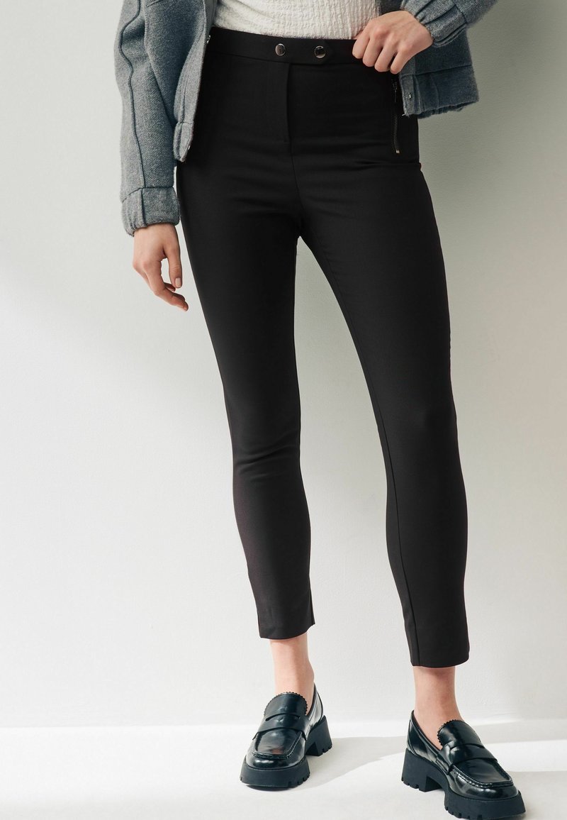 Černé kalhoty s vysokým pasem a slim fit, s předním zipovým zapínáním, dvěma knoflíky a dvěma bočními zipovými kapsami. Hladká, elastická látka.