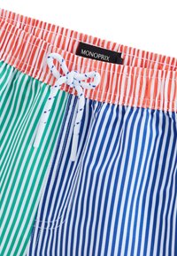 Shorts de bain rayés aux couleurs vert, bleu et corail. Taille élastique avec un cordon de serrage et des embouts en plastique blanc. L'étiquette indique "MONOPRIX."