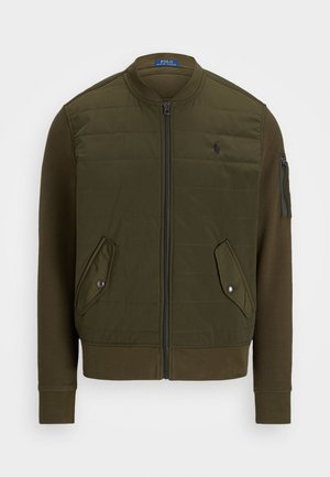 Oliivroheline pommitaja jakk, millel on tikkimine ees, täiskinnisega lukk, soonikkoes mansetid ja kaks eesmist taskut. Omab ka lukkudega käe taskut.