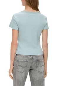 Jasnoniebieska, prążkowana koszulka z krótkim rękawem, z koronkowym wykończeniem przy kołnierzyku, wykonana z miękkiego materiału, w zestawieniu z jasnoszarymi dżinsami.