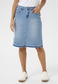 Fustă din denim albastru deschis, cu croială dreaptă, tiv sfâșiat și buzunare frontale. Dispune de un nasture metalic și închidere cu fermoar. Asortată cu teniși albi.
