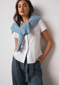 Biela košeľa s krátkym rukávom na gombíky v páre s svetlomodrým rebrovaným upleteným šálom omotaným okolo ramien. Tmavosivé nohavice so šnúrkami v páse.