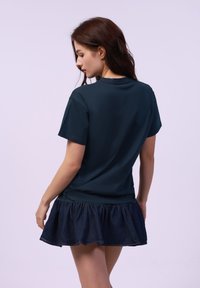 Camiseta de algodón azul marino con un corte relajado, combinada con una falda de mezclilla acampanada que presenta un dobladillo con volantes, vista desde la parte de atrás.