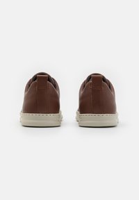 Brown leather sneakers with a seamless design, white rubber soles, and padded heel tabs. Minimal stitching and no visible logos.