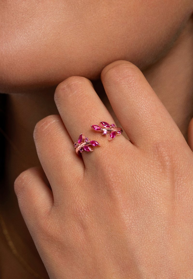 Anillo ajustable rosa con piedras preciosas rosa en corte marquise y pequeñas piedras transparentes, en un diseño de metal pulido curvado.